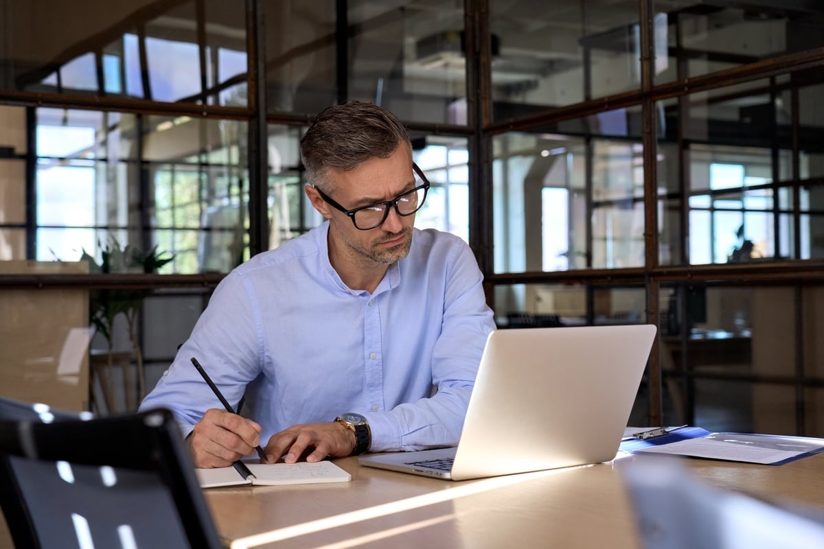 A man looking at his laptop taking notes