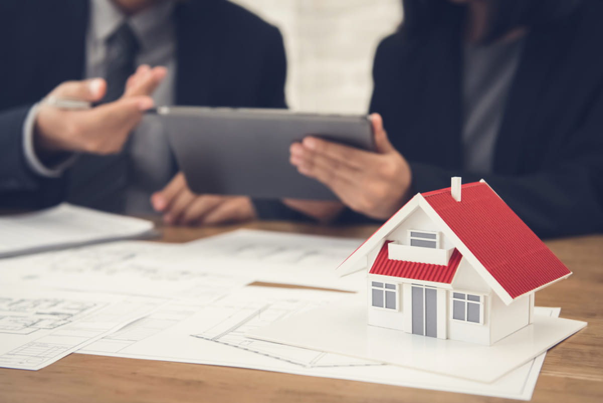 Business people review information on a tablet behind a model house, Seattle rental property management concept