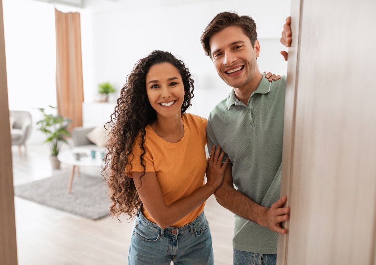 Portrait of excited cheerful couple inviting guest friends to enter their home