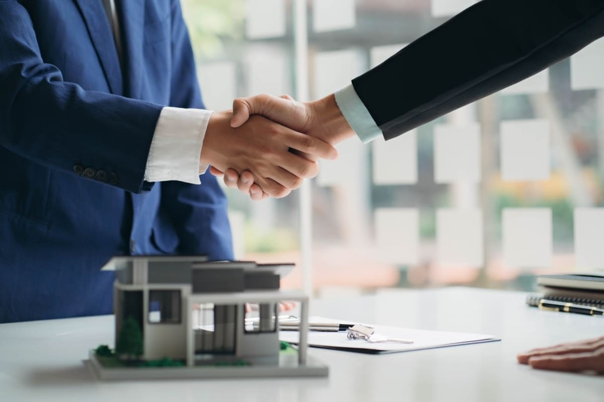 Two people shaking hands with a small home on the table, property management concept