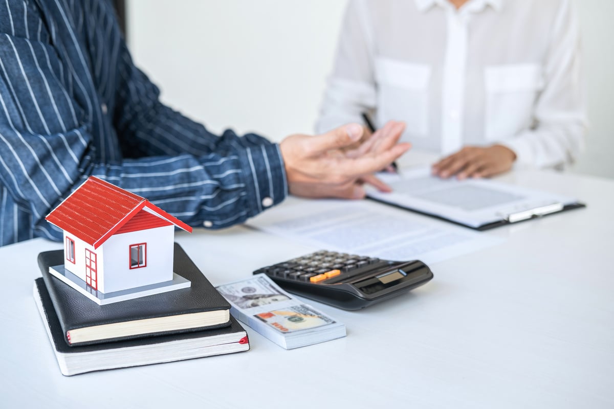 Two people talking next to a calculator, cash, and a miniature home