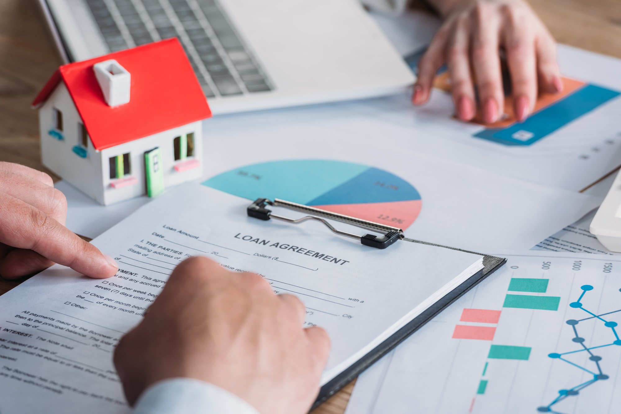 Partial view of man reading loan agreement while sitting at desk with graphs and charts near businesswoman