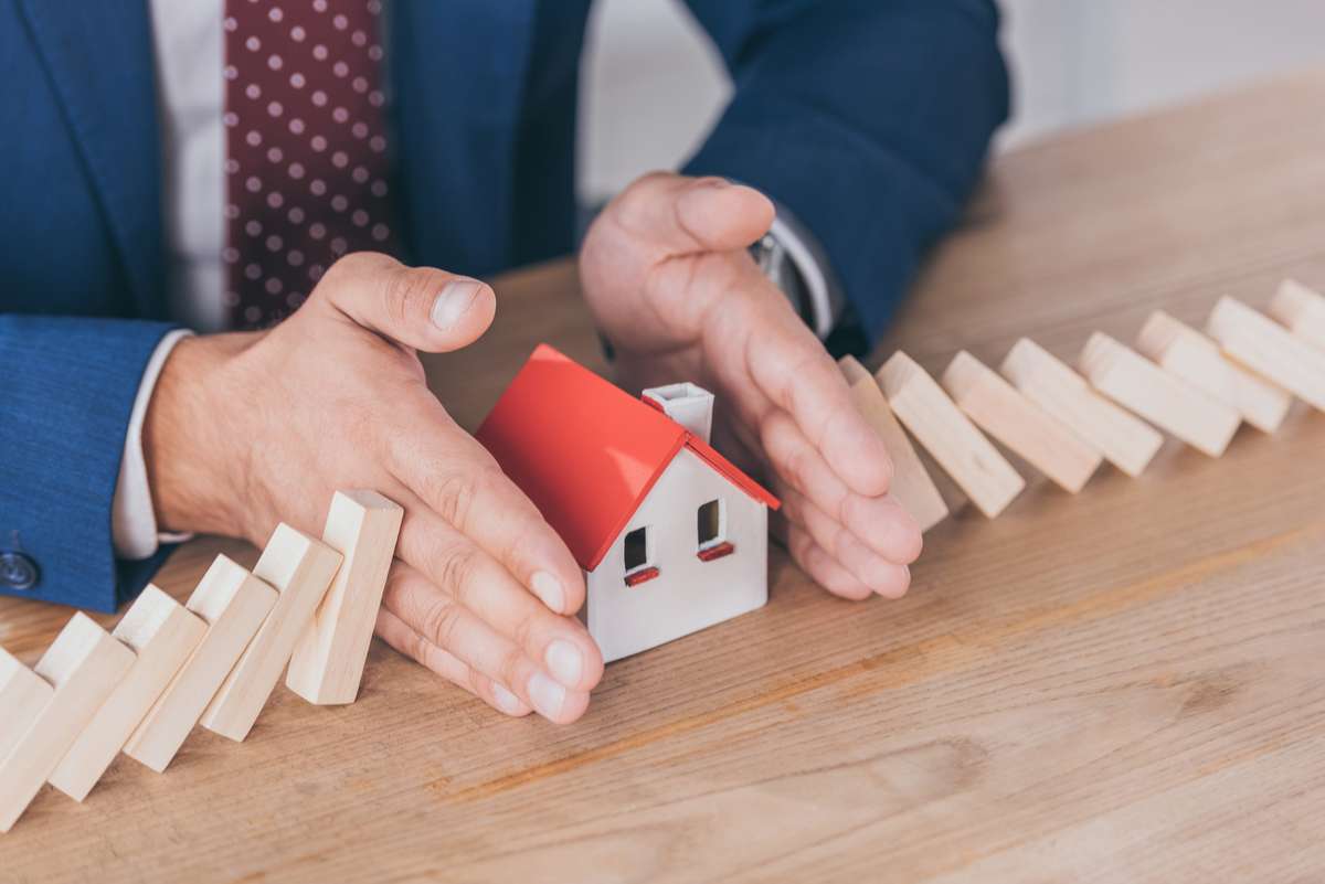 Cropped view of hands protecting a house from falling dominoes, Seattle property managers concept. 