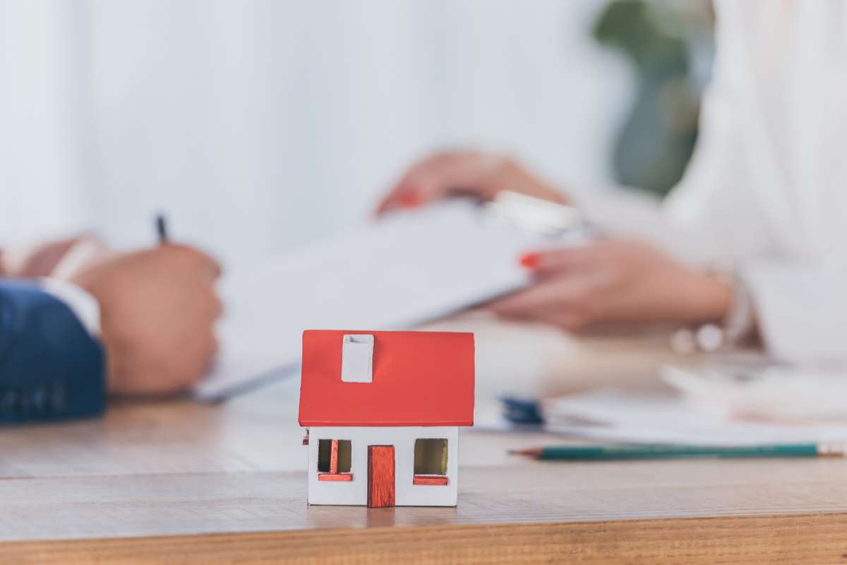 Selective focus of house model near businesswoman holding clipboard and client signing contract