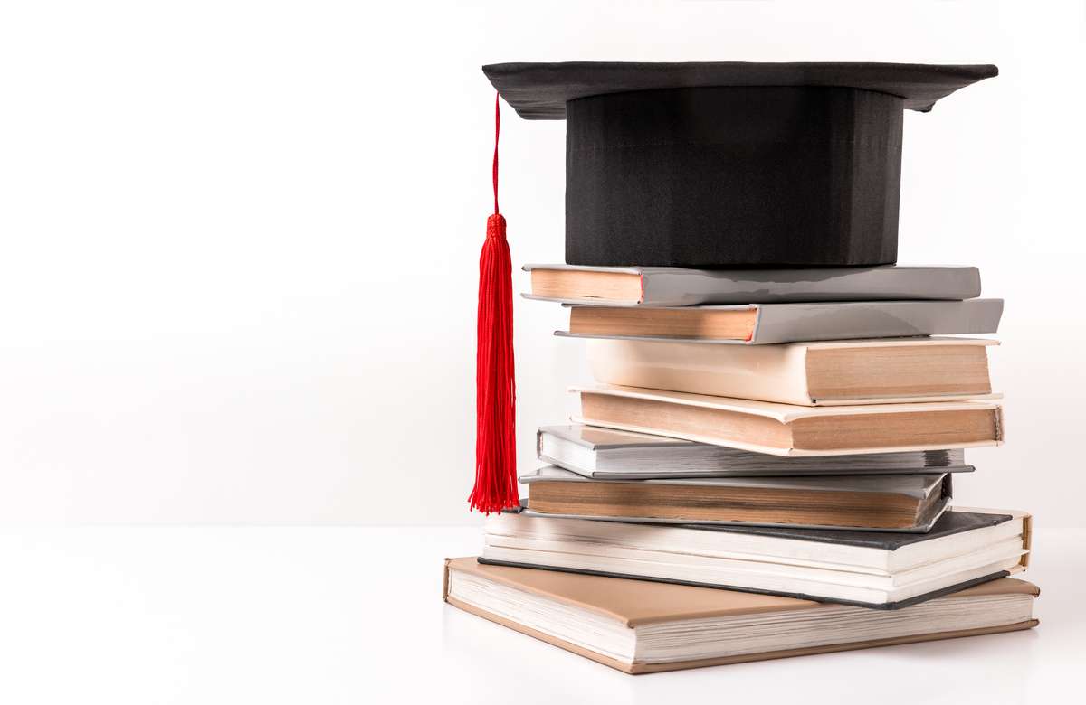 Square academic hat on stack of different books isolated on white