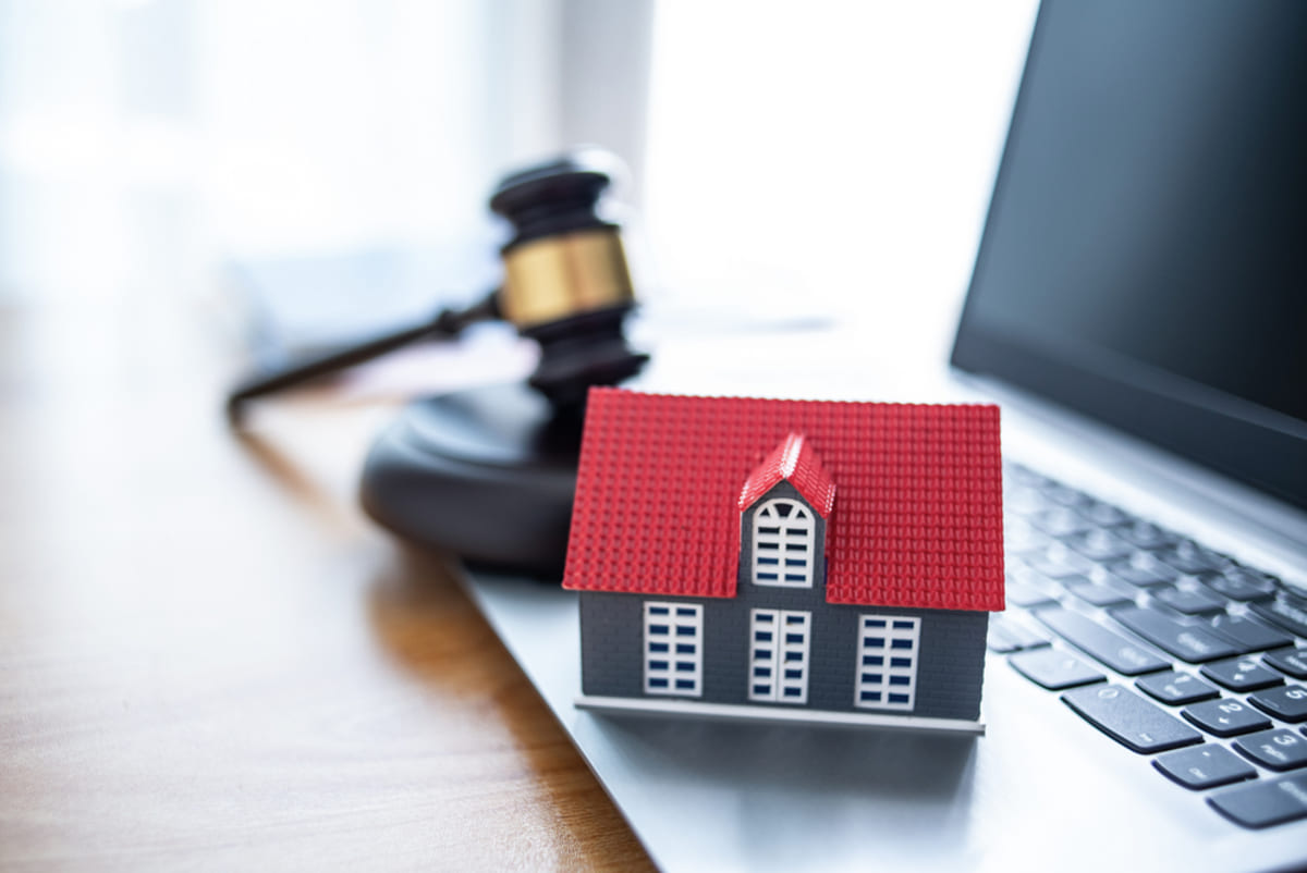 A small house on a laptop next to a gavel, regulatory compliance concept.