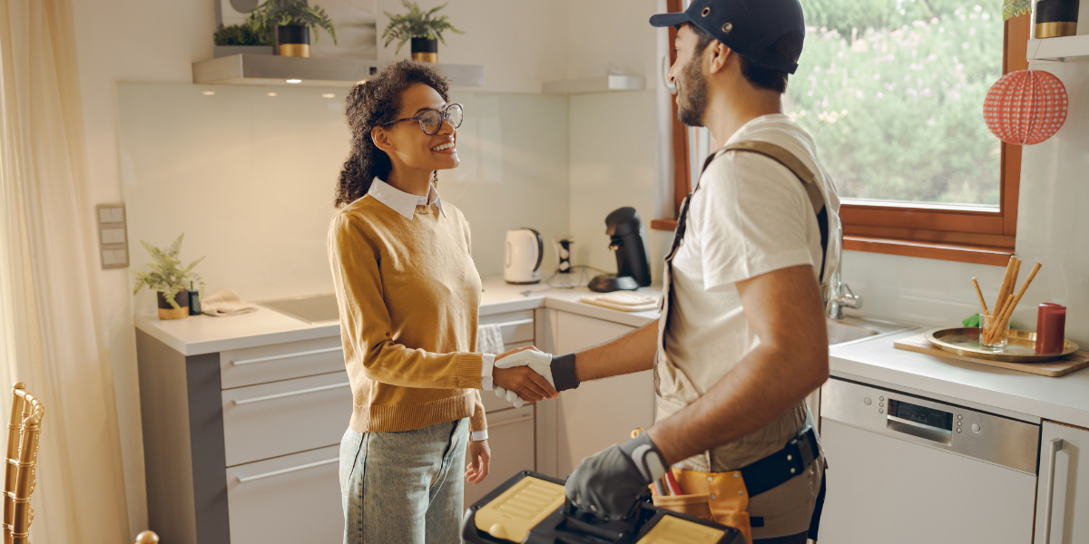 2 Professional repairman in uniform shaking hands with woman while standing at home kitchen